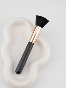 Flat top foundation brush with black soft bristles and gold ferrule on a white tray