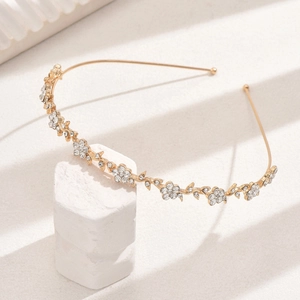 Detailed close-up of a gold floral headband with rhinestones on a white pedestal