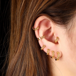 Detail of gold chain link earrings set including studs and cuffs on model ear
