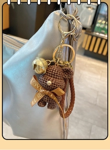 Close-up of brown resin bear keychain with gold bells on a silver fashion handbag