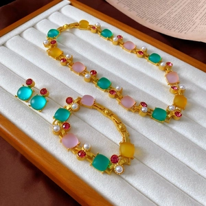 Vintage gold jewelry set featuring colorful square crystals and elegant pearls on white velvet