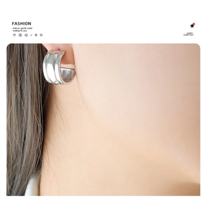 Close-up of a minimalist silver C-shaped earring with a polished metallic mirror finish