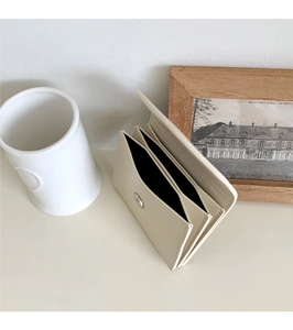 Detail showing the accordion fold structure and snap button of the cream card holder