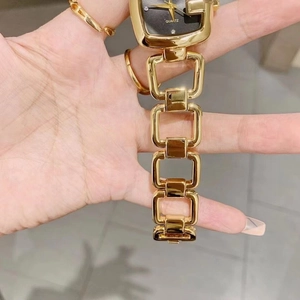 Close-up of a gold square watch with a hollow chain strap and black diamond dial