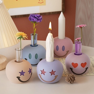 Detalle de jarrón de cerámica Morandi con cara sonriente y tubo de cristal en mesa