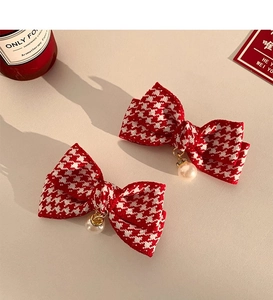 Close-up of red houndstooth bow hair clips with elegant pearl pendants on warm surface
