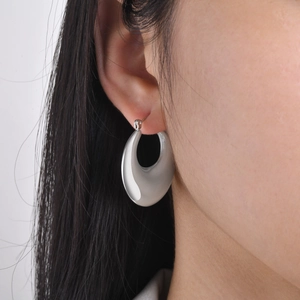 Close-up of polished silver hoop earrings worn on ear showing hollow geometric design
