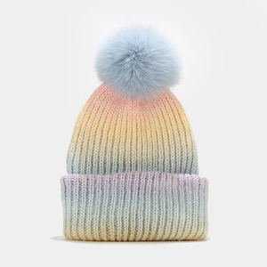 Détail du bonnet en tricot dégradé arc-en-ciel avec un pompon en fausse fourrure bleue