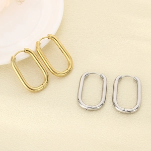 Detail of oval stainless steel hoop earrings in gold and silver on textured beige fabric