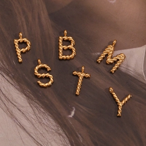 Detailed view of 18K gold plated twisted metal letter charms on a vintage background