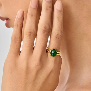 Detail of a gold-tone twisted ring featuring an oval green faux gemstone on a model's finger