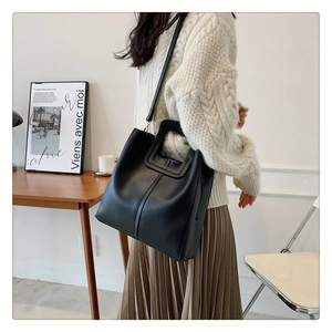 Dettaglio della borsa tote in pelle nera con manici robusti e trama liscia in luce soffusa