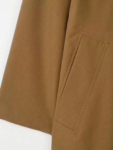 Close-up of brown trench coat showing high-quality twill fabric and pocket stitching detail