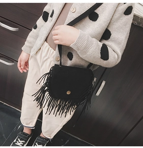 Detail showing the black fringe crossbody bag with gold buckle on a child model