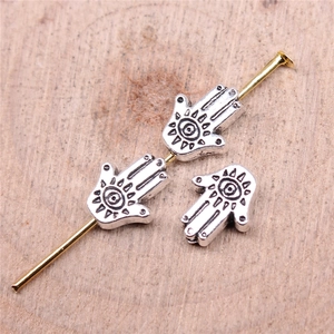 Antique silver Hamsa hand charm beads for vintage jewelry making on a wood background