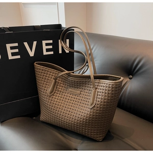 Detail of a brown woven tote bag with slim straps, displayed by a black paper bag