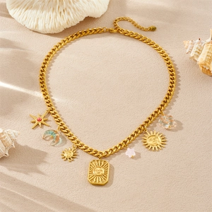 Detail of gold chain necklace featuring sun face and moon charms on sandy beach background