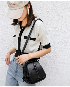 Close-up of black soft leather crossbody bag with multiple zippers worn by a model