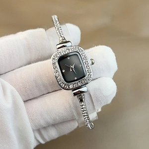 Close-up of silver square watch with black dial and crystal set strap on a gloved hand