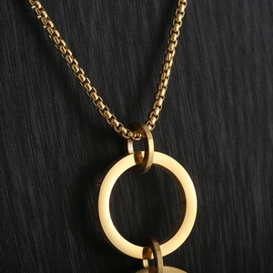 Macro detail of gold interlocking rings pendant on a textured black background
