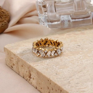 Detailed close-up of golden eternity ring featuring rectangular zircon stones on stone surface