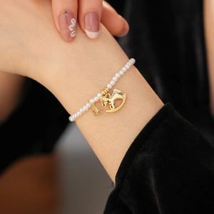 Detail view of a pearl bracelet with golden rocking horse and round coin charms on wrist