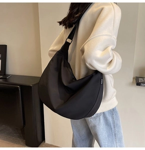 Detail shot of a large black waterproof crescent bag showing drape and fashion label