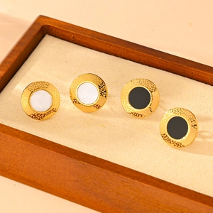 Golden titanium steel earrings with white and black round inlays on a wooden display tray