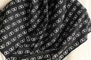 Detail of silk scarf showing white butterfly pattern on black satin fabric texture