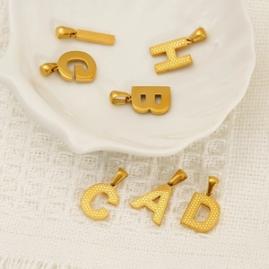 Elegant gold-plated stainless steel letter pendants displayed on a white ceramic shell tray