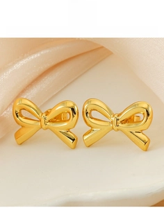 Macro detail of 18K gold titanium steel bow earrings on elegant silk fabric background