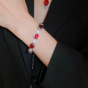 Close-up of a silver flower bracelet with red gemstones worn over a black blazer sleeve