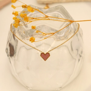 Macro detail of wine red heart pendant with gold bead trim on a delicate chain
