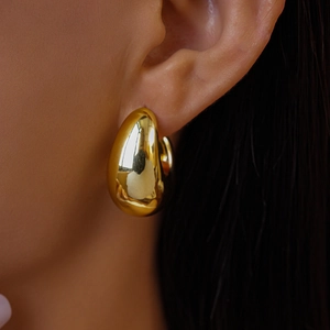 Close-up of polished gold chunky teardrop earrings worn by a model in a minimalist style