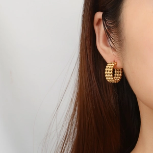 Close-up of golden C-shaped stainless steel earrings with woven mesh texture on model