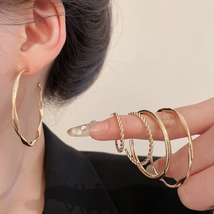 Close-up of golden twisted hoop earrings set showing various sizes on model and hand