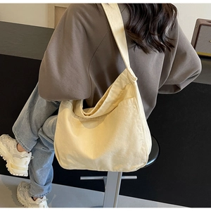 Side view of cream canvas crossbody tote bag on person showing large capacity and strap