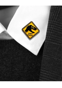 Macro detail of yellow warning sign enamel pin with black dinosaur and DON'T TOUCH text