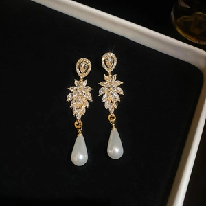 Macro detail of elegant leaf-shaped drop earrings with crystals and white teardrop pearl