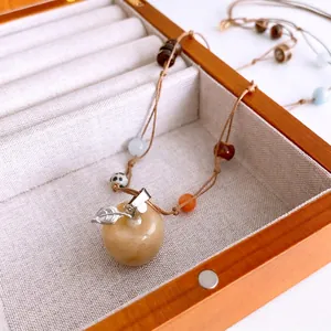 Handmade woven necklace with tiger eye stone apple pendant and beads on a wooden box