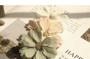 Close-up of three handmade fabric daisy flowers in cream, pink, and sage green shades