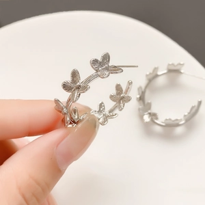 Detailed close-up of a silver-finish metal C-shaped hoop earring with a butterfly design