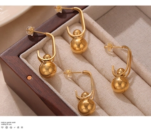 Detail of gold geometric earrings with steel spheres in a luxury wooden jewelry box