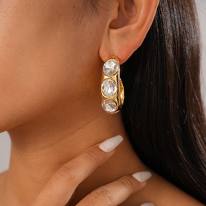 Detail view of large gold C-shaped hoop earrings with three inlaid clear round gemstones