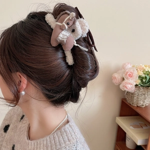 Close-up of a plush pony-shaped hair claw clip worn by a model in a cozy indoor setting