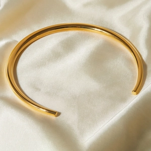 Close-up of minimalist gold metal choker collar on elegant white silk fabric