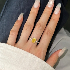 Close-up of radiant cut yellow gemstone ring with silver diamond pavé band on finger
