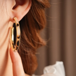 Close-up of golden C-shaped hoop earrings with leopard print resin on model's ear