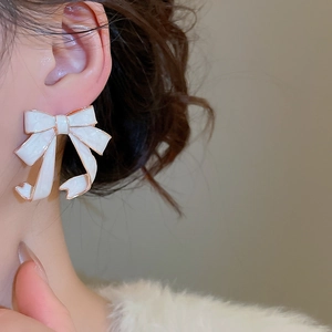 Detail of white enamel bow earrings with gold trim worn for an elegant feminine look
