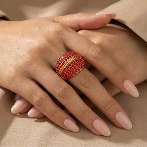 Close-up of wide gold ring with red rhinestones worn on finger over khaki fabric